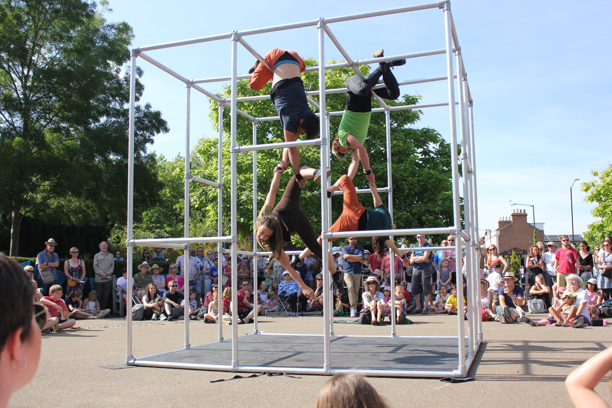 Two performers suspend themselves by their hips from high up poles, while holding two other performers off the ground.