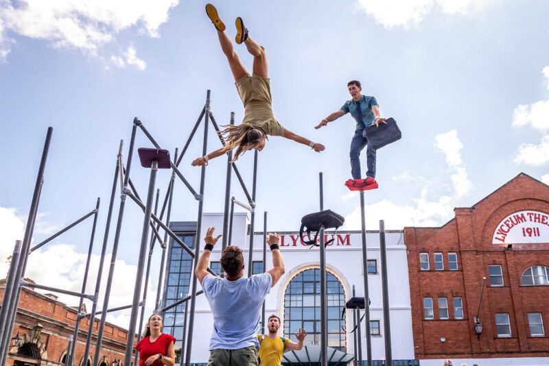 An image of a group of performers jumping from a large steel frame structure.