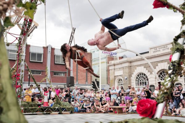 An image of two male trapeze artists hanging from a fixed point and flying through the air with a crowd below.