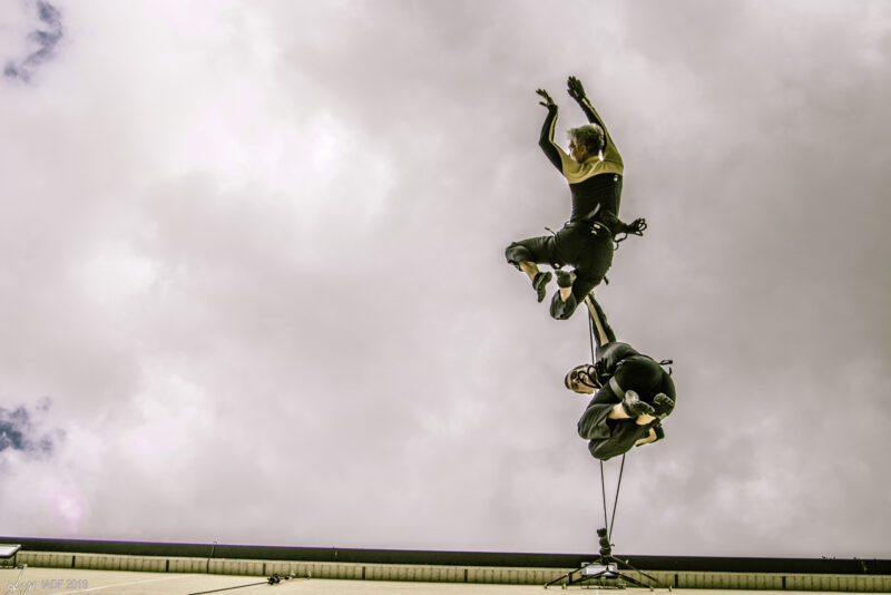 An image of two trapeze artists against a cloudy sky background.