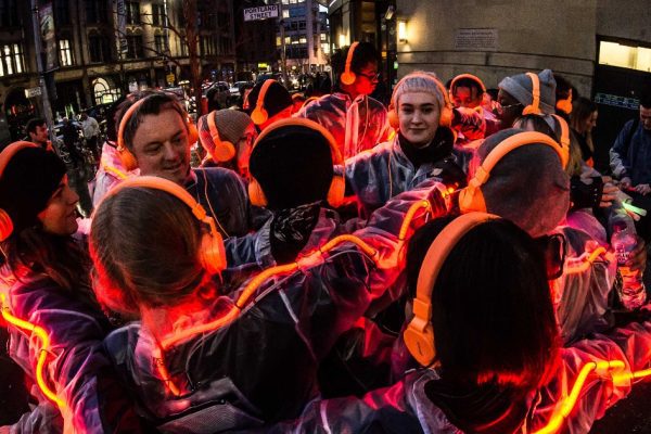 A night time image of a group of people huddled in a circle wearing headphones and surrounded by an orange wire of light.