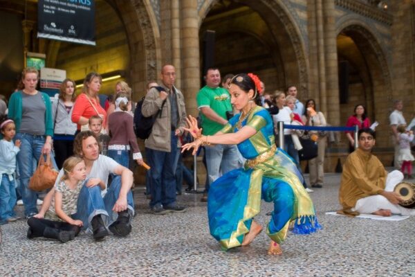 An image of a female South Asian dancer wearing traditional Indian blue and gold dress surrounded by a small crowd.