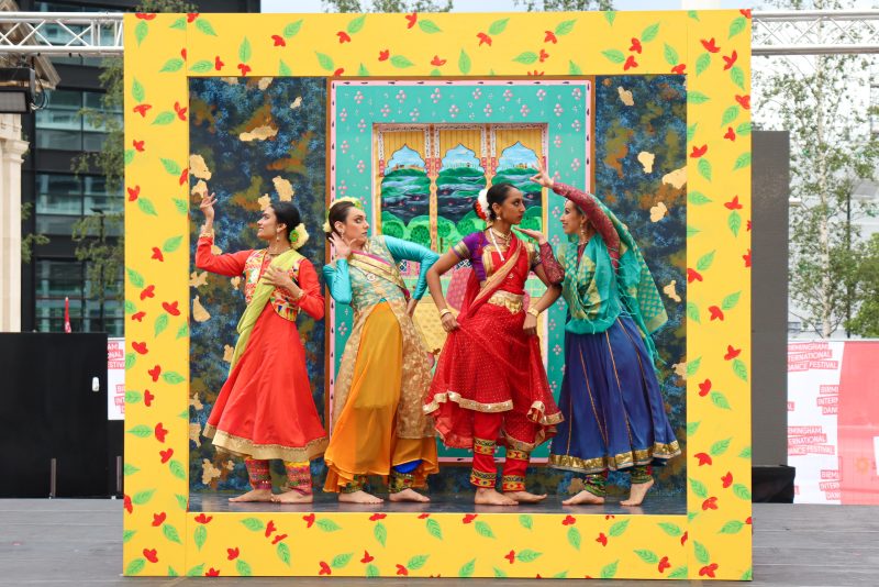 An image of four South Asian female dancers stood inside a large frame wearing traditional Indian dress