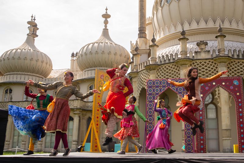 An image of a group of female dancers with a mosque or temple behind them. They are wearing traditional Indian dress