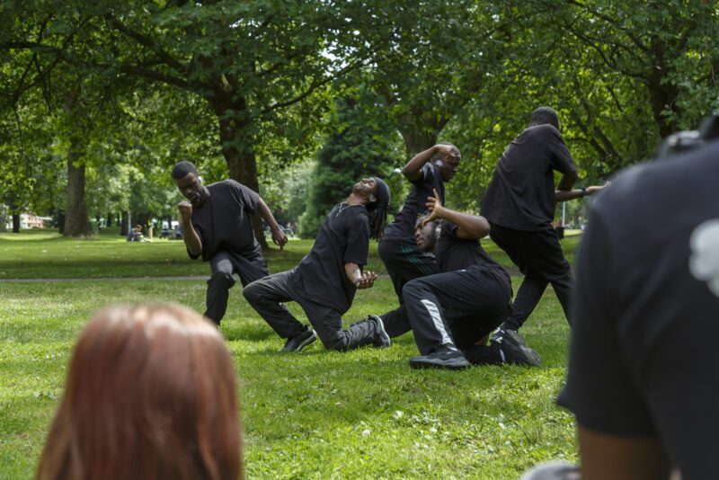 An image of a group of male performers dressed in black on a grassy area.