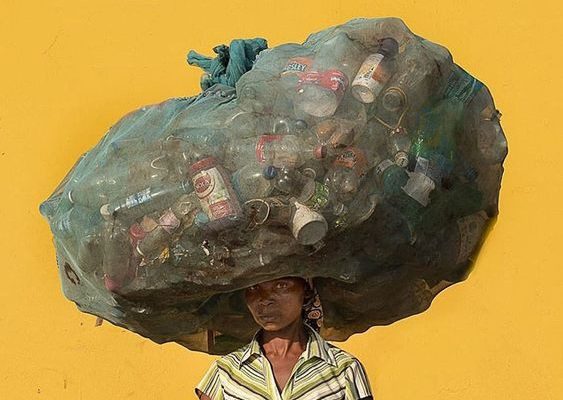 Balance. An image of a woman balancing a bag of rubbish on her head with a yellow background.