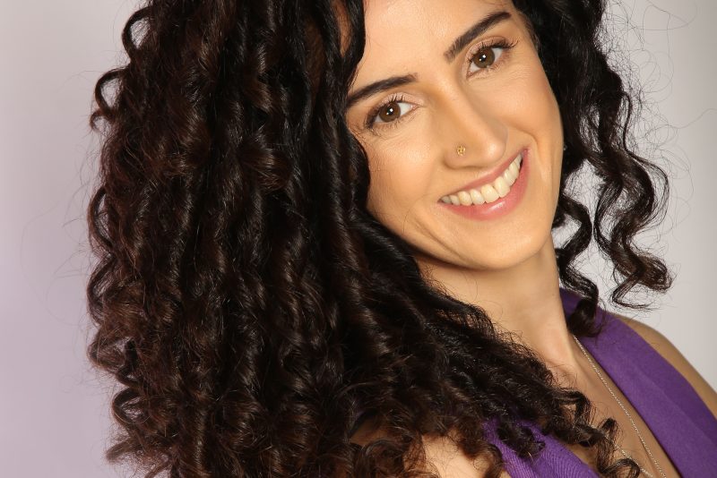 Colour image of a woman with long dark curly hair smiling at the camera.