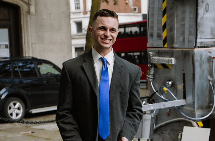 A portrait image of a young man wearing a suit with a bright blue tie.