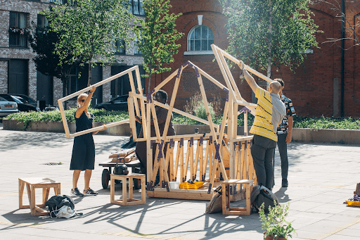 Township explores our relationship with food and shelter, bringing people together in one feast experience. An image of a group of people building a wooden structure in the street.