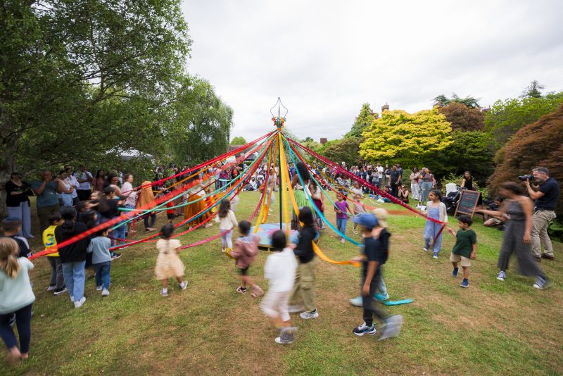 An image of a maypole with people dancing around it.
