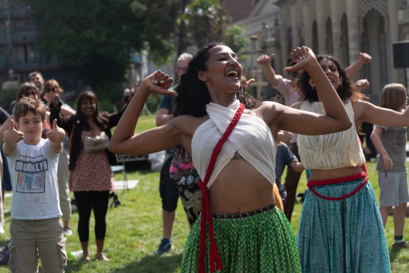 An image of two female dancers wearing traditional Indian clothing and an audience copying their pose in the background.