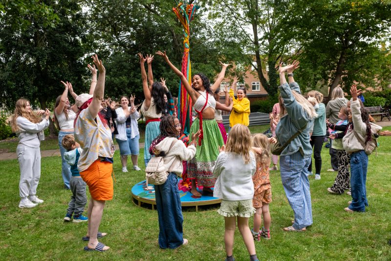 An image of a female dancer stood on a circular wooden platform surrounded by an audience.