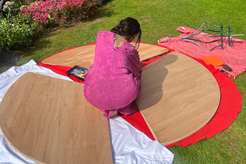 A image of a female crouched down on the floor surrounded by circular pieces of wood.