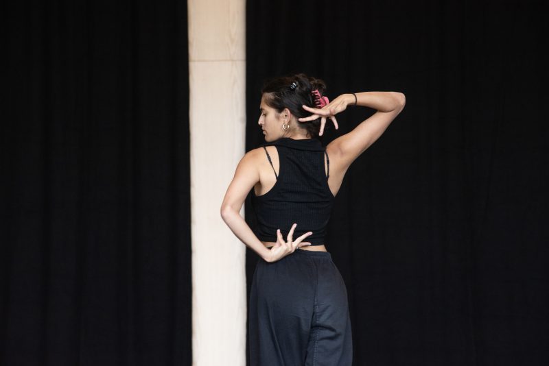 An image of a female dancer with her back to the camera against a dark background.