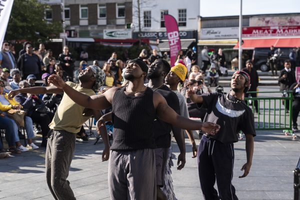 A group of black male dancers perform to a street crowd.
