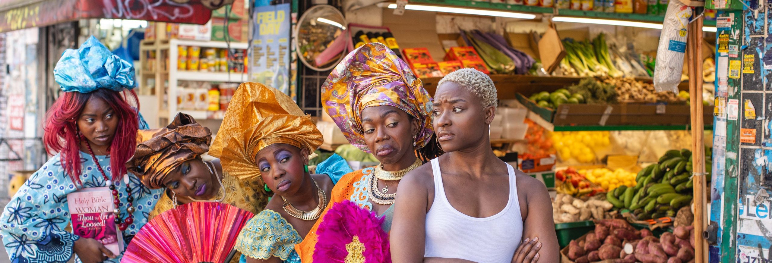An image of five black women stood outside a fresh grocery store. Four of the women are wearing traditional African dress.