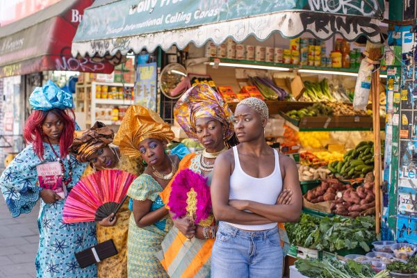 An image of five black women stood outside a fresh grocery store. Four of the women are wearing traditional African dress.