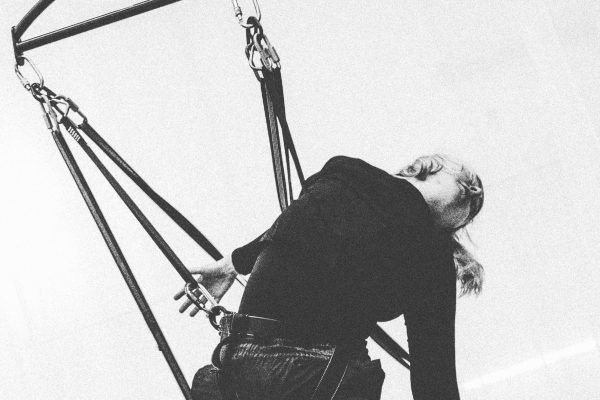A black and white image of a female trapeze artists swinging from a makeshift swing.